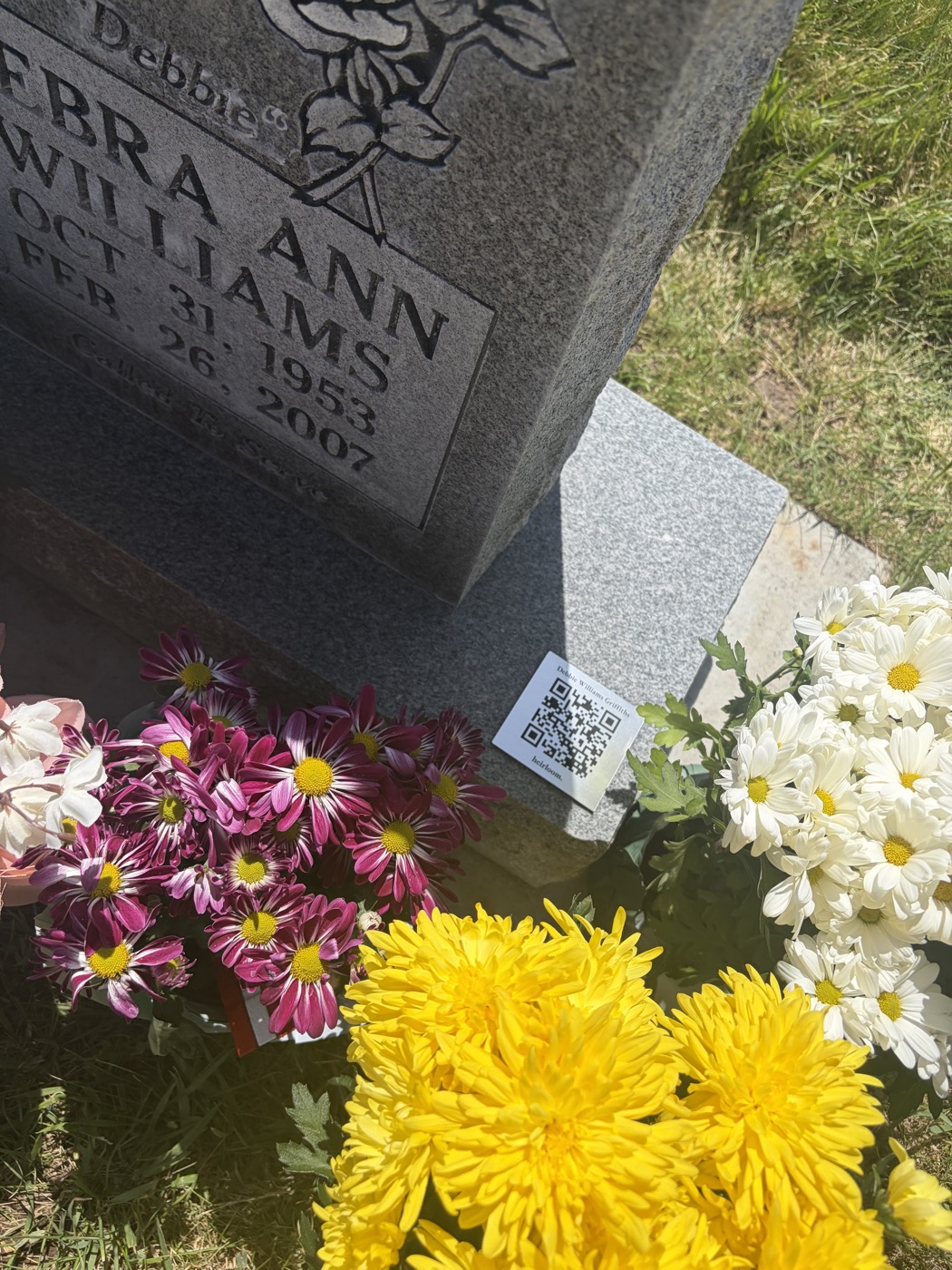 Close-up of an Heirloom marker on a granite headstone surrounded by fresh chrysanthemums.